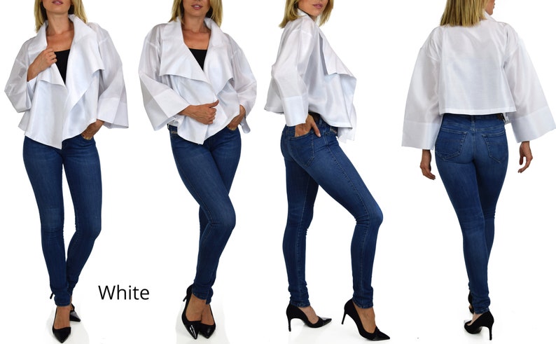 May include: A white, lightweight, cropped jacket with a draped, asymmetrical design. The jacket has long sleeves with wide cuffs and a relaxed fit. The model is wearing the jacket with blue jeans and black heels.