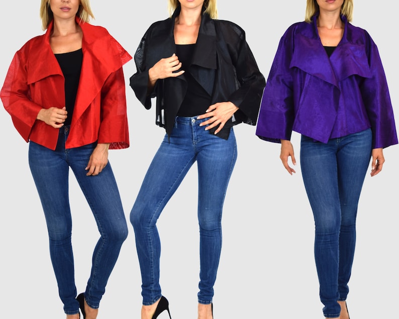 May include: Three women are wearing different colored jackets. The jackets are all made of a sheer fabric and have a draped collar. The women are wearing blue jeans.