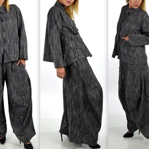 May include: A two-piece outfit in a gray and black striped fabric. The jacket has a mandarin collar and long sleeves. The pants are wide-legged and have a loose fit.