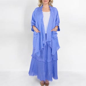 以下が含まれることがあります： フリンジの裾とポケットが付いた青いリネンジャケット。ジャケットは白いTシャツと青いティアードスカートの上に着用されています。