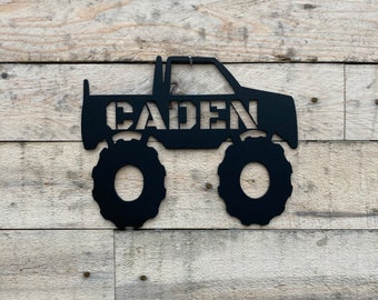 May include: Black metal monster truck cutout with the name CADEN cut out of the truck. The truck has large tires and a flatbed.