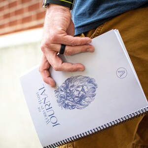 May include: A white journal with a blue lion illustration and the text "WORD IN HABIT JOURNAL" on the cover. The journal has a black spiral binding.