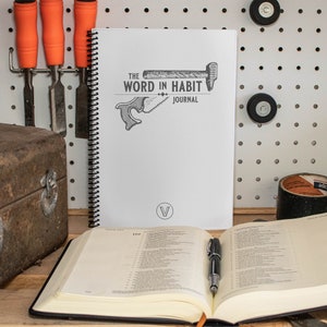 May include: A white spiral bound journal with the text "The Word in Habit Journal" and a black and white illustration of a hammer and saw. The journal is open to a page with the number 119.