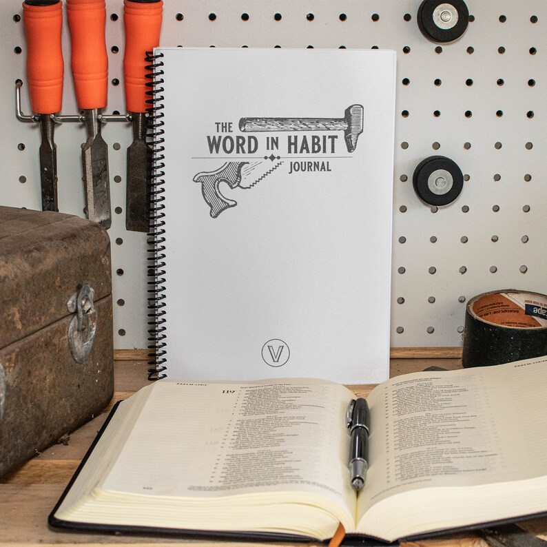 May include: A white spiral bound journal with the text "The Word in Habit Journal" and a black and white illustration of a hammer and saw. The journal is open to a page with the number 119.
