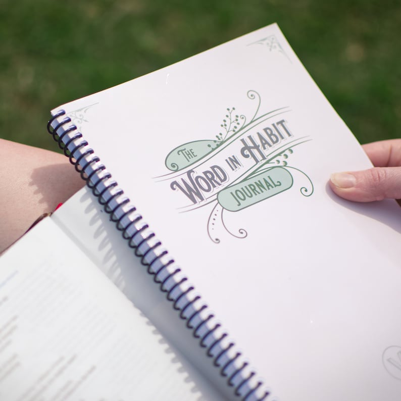 May include: A white spiral bound journal with the text "The Word in Habit Journal" in green and gray lettering with a decorative floral design.