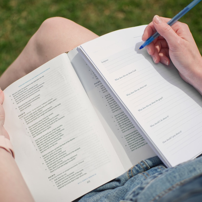 May include: A person sits on the grass and reads a Bible with a journal open in their lap. The journal has prompts for reflection on the Bible passage. The prompts include "What does this say about God?", "What does this say about me?", "What does this say about the people?", "What should I do about it?", and "How should I pray about it?"