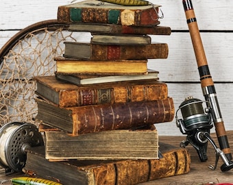 May include: A stack of weathered, antique hardcover books with worn leather spines, topped with a green and yellow fishing lure. A fishing rod with a reel, a circular net, and additional colorful fishing lures are arranged around the books.