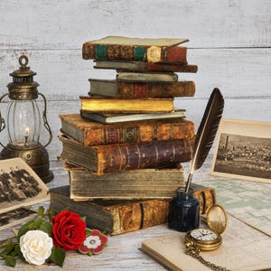 Può includere: Una pila di libri antichi rilegati in pelle, un calamaio blu scuro con una penna d'oca nera, una lanterna in ottone, un orologio da taschino dorato, una fotografia vintage e rose rosse e bianche su documenti e una mappa.