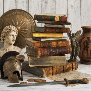 May include: A stack of antique leather-bound books, a bronze-colored Corinthian helmet, a stone bust of a person, a circular shield, a winged statue, a terracotta vase, a metal sword, and several gold coins arranged on a white wooden surface.