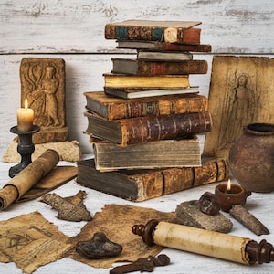 May include: A stack of weathered, antique books with worn leather covers and aged pages, surrounded by two lit candles in dark holders, a rolled parchment scroll, scattered fragments of old paper, and a small, dark ceramic pot.