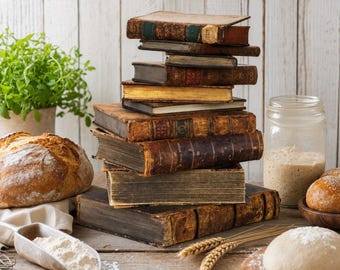 May include: A vertical stack of eight antique, weathered hardcover books with worn brown and dark leather spines. The books are arranged in a column, showcasing aged pages and textured covers, positioned alongside a loaf of bread and dough.