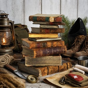 May include: A stack of weathered, leather-bound antique books sits centrally, surrounded by a metal lantern with a lit flame, a folding knife, a brass compass, a pair of brown leather boots, a green backpack, and a first aid kit with a white cross.