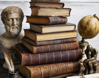 May include: A stack of ten antique leather-bound books sits beside a stone bust of a bearded man, a bronze globe, a bronze inkwell with a feather quill, a metal letter opener, and a rolled parchment scroll tied with twine on a wooden surface.