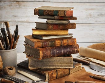 Peut inclure: Une pile verticale de livres anciens reliés en cuir aux bords usés et aux dos visibles, accompagnée de divers outils de reliure dont des poinçons en métal, un plioir, une bobine de ficelle et un morceau de cuir brun sur une surface en bois.