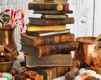 May include: A vertical stack of antique, leather-bound books with worn spines and gilded edges. Surrounding the books are various chocolate truffles, square caramels, and red and white striped candy canes in a brass vessel.