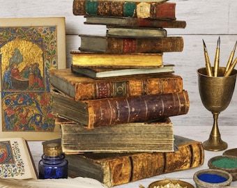 Può includere: Una pila di libri antichi rilegati in pelle con pagine dai bordi dorati, un calamaio in vetro blu, una penna d'oca bianca, un calice in ottone con tre pennini metallici, un piattino con foglia d'oro e ciotole di pigmenti accanto a un manoscritto.