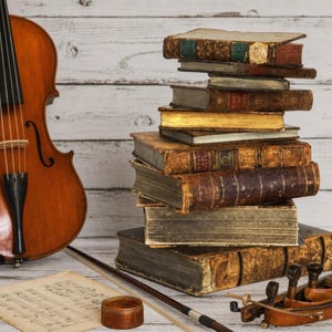May include: A wooden violin with a bow, a stack of antique leather-bound books with gold-edged pages, a small round wooden container, and a sheet of musical notation. The violin features a dark brown finish, black tuning pegs, and a black tailpiece.