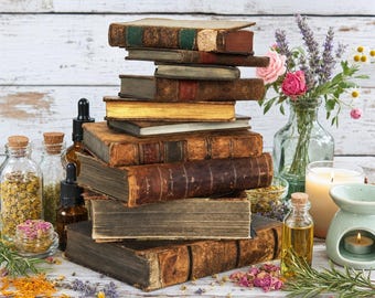 Könnte beinhalten: Ein Stapel aus neun antiken, ledergebundenen Büchern steht neben einer Glasvase mit Lavendel und Rosen, mehreren Braunglasflaschen mit Pipetten, einem kleinen Glas mit getrockneter Kamille und einer Keramik-Duftlampe mit Teelicht.