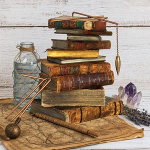 May include: A stack of antique leather-bound books with gold-edged pages, a clear glass bottle wrapped in twine, two copper dowsing rods, a brass pendulum on a chain, a wooden wand, and raw amethyst crystals resting on a vintage map.