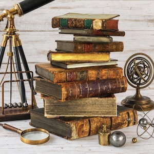 Puede incluir: Una pila de libros antiguos encuadernados en cuero se encuentra en el centro, flanqueada por un telescopio de latón sobre un trípode, una cuna de Newton de metal, una lupa, una esfera armilar de latón, un pequeño peso de latón y un modelo de esfera.