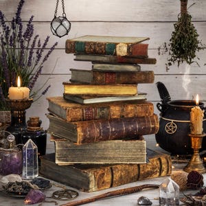 Pode incluir: Uma pilha de livros antigos e desgastados com lombadas de couro e páginas envelhecidas. Ao redor dos livros há um caldeirão preto, duas velas acesas em suportes, cristais de quartzo, uma pedra roxa, um pentáculo e ervas secas.