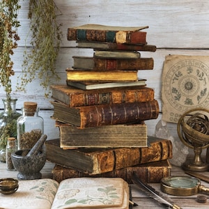 Peut inclure: Une pile de livres anciens reliés en cuir patiné est disposée à côté d'un bocal en verre contenant des herbes séchées, un mortier en pierre, un journal botanique ouvert, une loupe en laiton et une sphère armillaire sur une surface en bois.