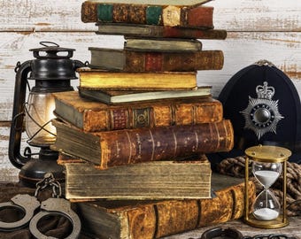 May include: A stack of weathered antique books sits beside a black metal lantern, a dark blue police helmet with a silver badge, a brass hourglass with white sand, and metal handcuffs with a chain on a rustic wooden surface.