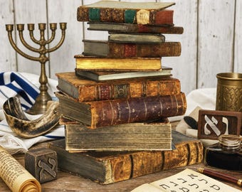 May include: A stack of antique, weathered books with worn leather covers and gold-edged pages. Beside the stack are a brass menorah, a shofar, a scroll with Hebrew text, a wooden block with the Hebrew letter Aleph, and an open notebook with Hebrew characters.