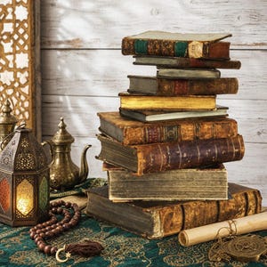 May include: A stack of antique hardcover books with worn leather spines and aged pages, accompanied by a brass lantern with colored glass panels, a metallic teapot, a string of wooden prayer beads, and a rolled parchment scroll on a green cloth.