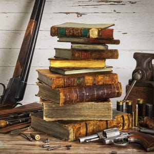 May include: A stack of antique, leather-bound books with weathered pages and gold-gilded edges. Beside the books are a long-barreled shotgun, a metal bench vise, a silver revolver, various brass bullet casings, and small metal cleaning tools.