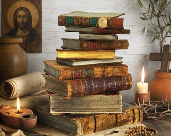 May include: A vertical stack of antique, leather-bound books with worn edges and gold-gilded pages. The collection includes volumes with textured spines, aged paper, and visible wear, resting on a wooden surface alongside a rosary and candles.