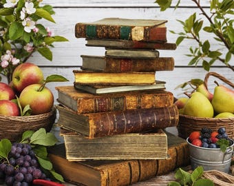 May include: A vertical stack of antique hardcover books with worn brown and gold spines, surrounded by baskets of red apples and yellow pears, a small metal bucket of mixed berries, a cluster of purple grapes, and red-handled pruning shears.