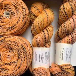May include: Three skeins of hand-dyed yarn in a bright orange and black colorway. The yarn is labeled "Delightful" and is a House Twist (2ply) made of 100% Peruvian Highland Wool. The label also states that the yarn is non-superwash and has 437 yards per 100 grams.