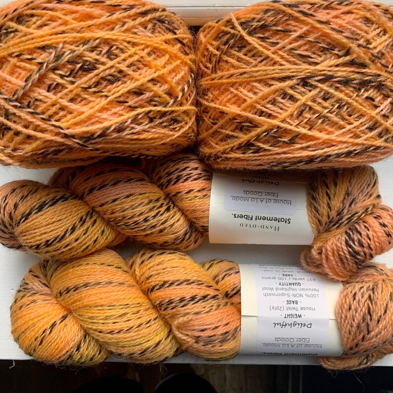 May include: Two skeins of hand-dyed yarn in a bright orange and black colorway. The yarn is labeled "Delightful" and is a House of A La Mode Statement Fibers yarn.