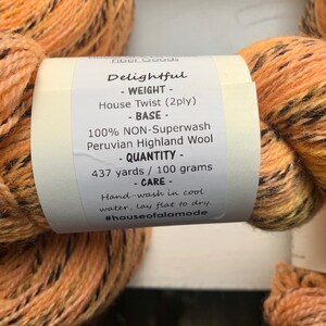 May include: A skein of orange and black yarn labeled "Delightful" with the details: "House Twist (2ply)", "100% NON-Superwash Peruvian Highland Wool", "437 yards / 100 grams", "Hand-wash in cool water, lay flat to dry." and the hashtag "#houseofalamode".
