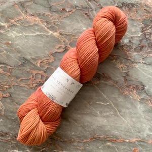 May include: A skein of coral colored yarn with a white label that reads "Le Feu Poussiere, Hand dyed and hand-knitted, Quebec, Canada."