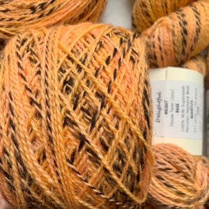 May include: A skein of orange and black yarn with the label "Delightful" and "Base" printed on it. The yarn is 100% wool and is a worsted weight.