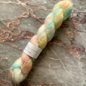 May include: A skein of soft, multi-colored yarn with shades of pink, yellow, and blue. The yarn is made of mohair and silk and is 500 yards long.