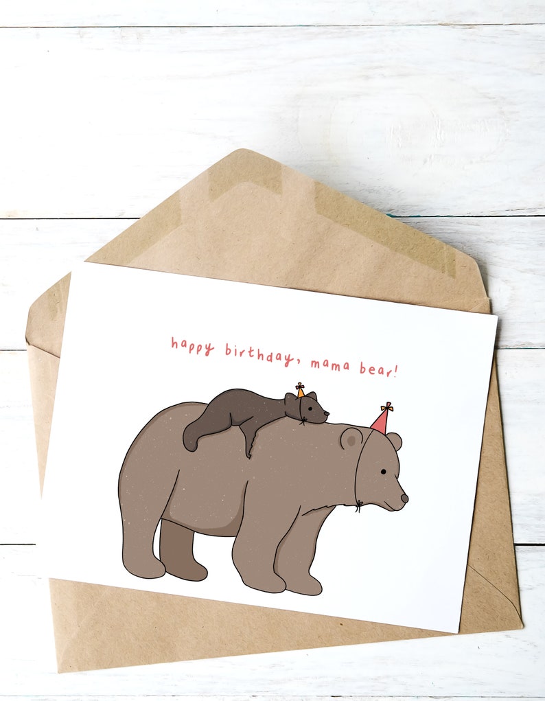 Pu&ograve; includere: Biglietto di compleanno in una busta marrone. La carta presenta un'illustrazione a cartoni animati di un grande orso marrone con un orso pi&ugrave; piccolo sulla schiena, entrambi con cappelli da festa. Il testo "happy birthday, mama bear!" &egrave; scritto in rosso.