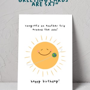 K&ouml;nnte beinhalten: Eine wei&szlig;e Gru&szlig;karte mit dem Text "GREETING CARDS ARE 5X7" oben. Die Karte zeigt eine l&auml;chelnde Sonne mit einer Erdengrafik und den S&auml;tzen "congrats on another trip around the sun!" und "happy birthday!"