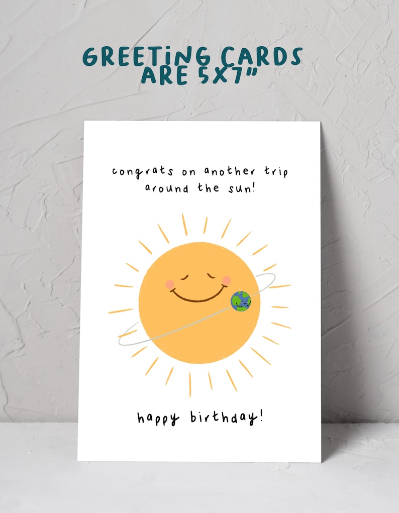 K&ouml;nnte beinhalten: Eine wei&szlig;e Gru&szlig;karte mit dem Text "GREETING CARDS ARE 5X7" oben. Die Karte zeigt eine l&auml;chelnde Sonne mit einer Erdengrafik und den S&auml;tzen "congrats on another trip around the sun!" und "happy birthday!"