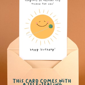 K&ouml;nnte beinhalten: Geburtstagskarte mit einem l&auml;chelnden Sonnengesicht und der Erde, die es umkreist. Der Text lautet: "Herzlichen Gl&uuml;ckwunsch zu einer weiteren Reise um die Sonne!" und "Alles Gute zum Geburtstag!" Mit selbstklebendem Umschlag.