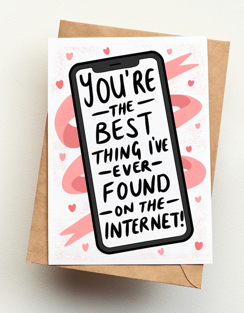 Op de afbeelding: Een wenskaart met een bruine envelop. De kaart toont een smartphone-afbeelding met de tekst "You're the best thing I've ever found on the internet!" in het zwart. Roze harten en een roze lint accentueren de witte achtergrond.