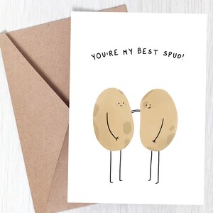 May include: A greeting card with the text "YOU'RE MY BEST SPUD!" features two cartoon potatoes with arms and legs. The potatoes are light brown with dark brown spots. A brown envelope is in the background.