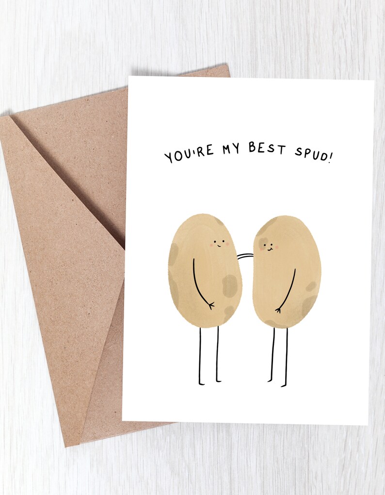 May include: A greeting card with the text "YOU'RE MY BEST SPUD!" features two cartoon potatoes with arms and legs. The potatoes are light brown with dark brown spots. A brown envelope is in the background.