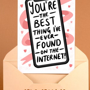 Op de afbeelding: Een wenskaart met een smartphone-afbeelding met de tekst "You're the best thing I've ever found on the internet!". De kaart zit in een perzikkleurige envelop met de tekst "Self-sealing envelope included". Roze hartjes en een lint versieren de kaart.