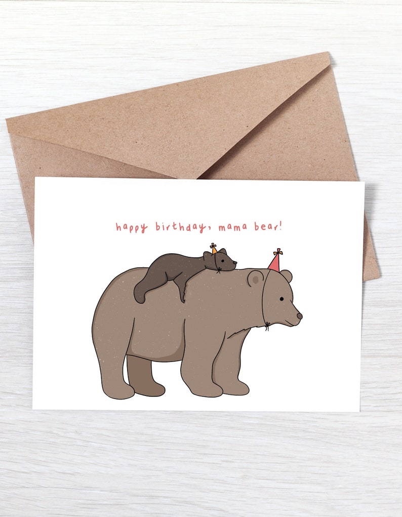 Pu&ograve; includere: Un biglietto di auguri con una busta marrone. Il biglietto presenta un'illustrazione a cartoni animati di un grande orso marrone con un orso pi&ugrave; piccolo sulla schiena, entrambi con cappelli da festa. Il testo "happy birthday, mama bear!" &egrave; scritto in rosso.