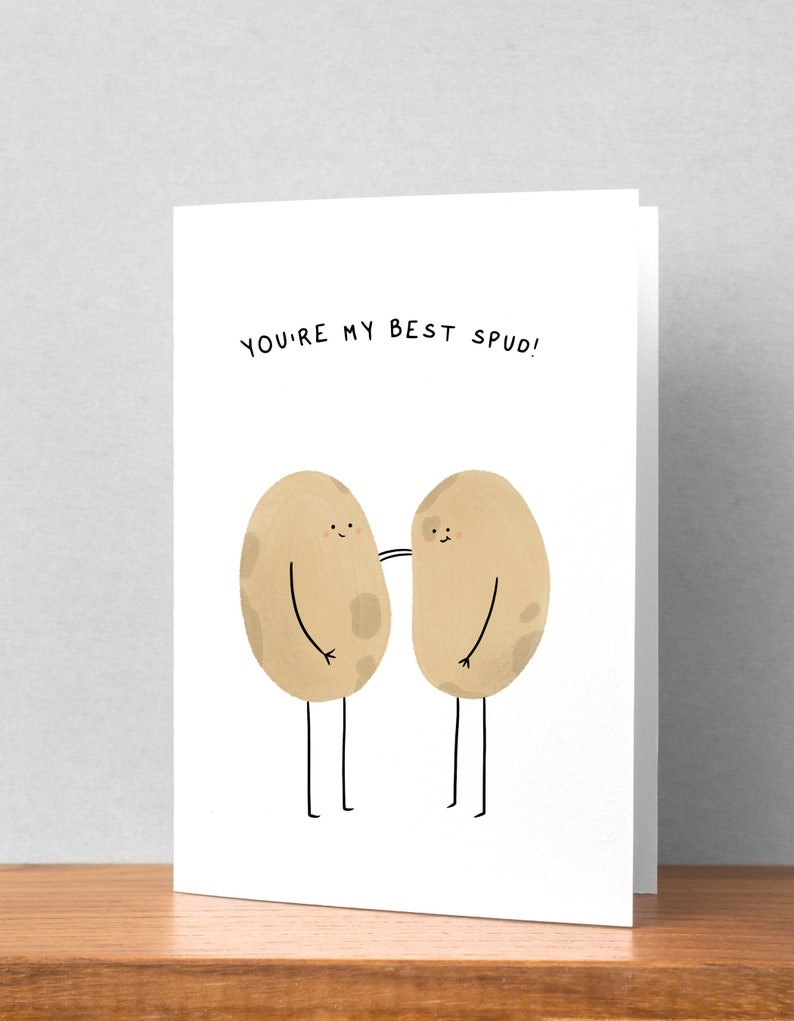 May include: A white greeting card with the text "YOU'RE MY BEST SPUD!" above two cartoon potatoes with arms and legs. The potatoes are light brown with small brown spots and are touching each other.