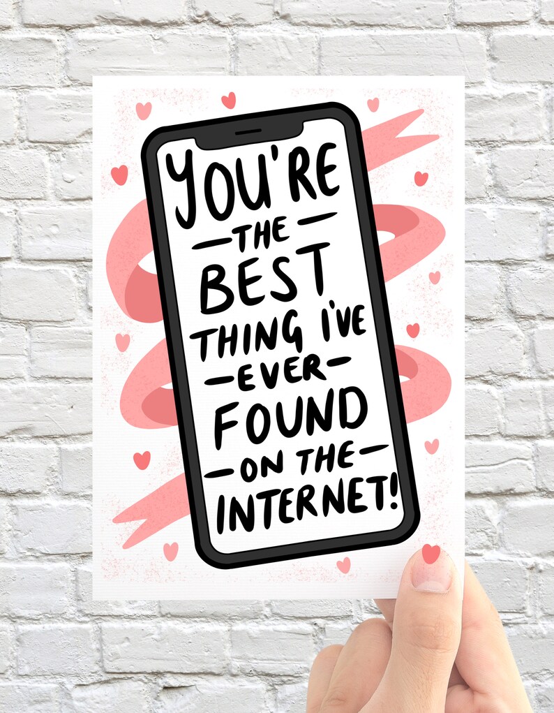 Op de afbeelding: Een wenskaart met een smartphone-illustratie en de tekst "You're the best thing I've ever found on the internet!" in het zwart. De kaart heeft een witte achtergrond met roze hartjes en linten.