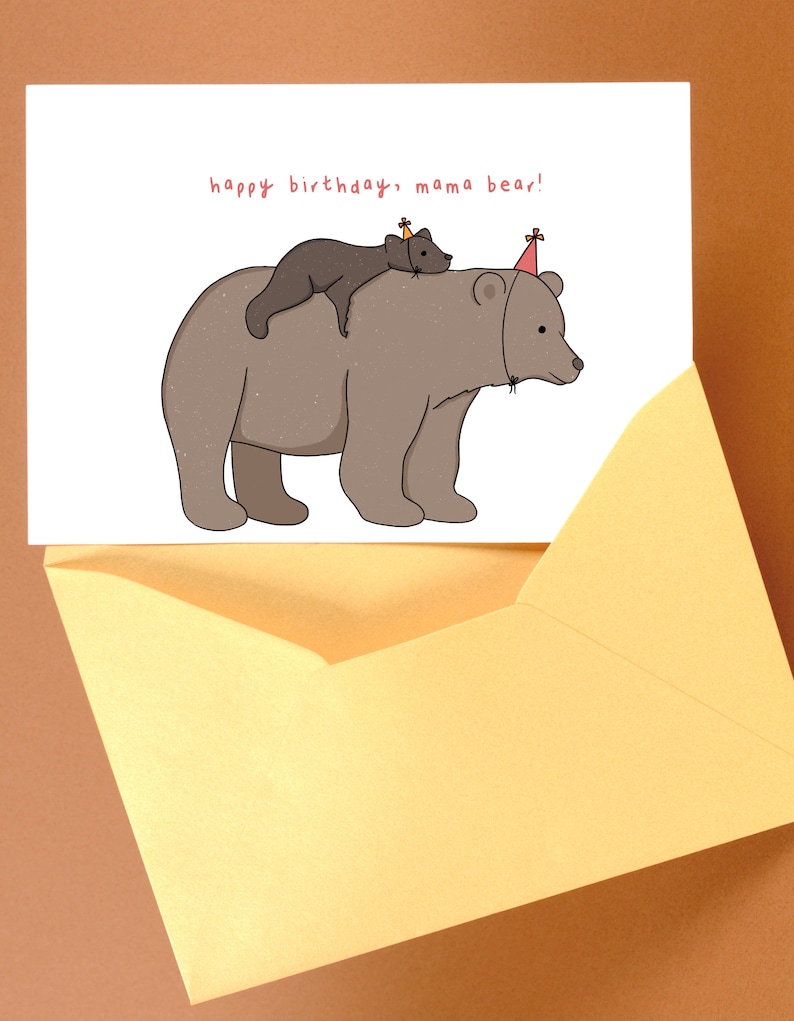 Pu&ograve; includere: Un biglietto di compleanno con un'illustrazione a cartoni animati di un grande orso marrone con un orso pi&ugrave; piccolo sulla schiena, entrambi con cappelli da festa. Il biglietto dice "happy birthday, mama bear!" ed &egrave; in una busta gialla.